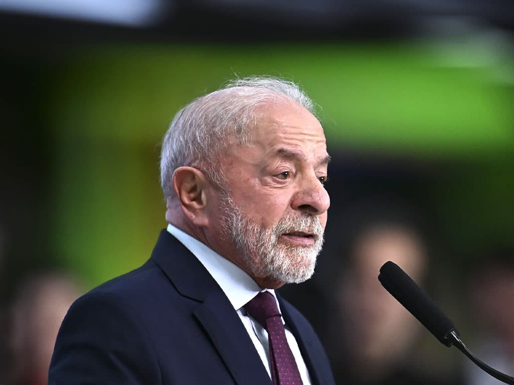 Luiz Inácio Lula da Silva, de terno escuro, camisa branca e gravata vinho, fala ao microfone de perfil.